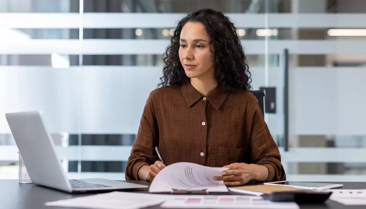 A woman looking at the laptop screen and taking notes.