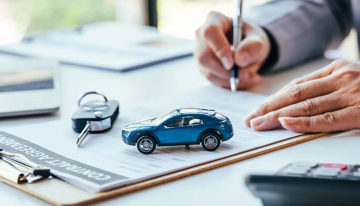 An image of a hand signing a document next to a car key fob.