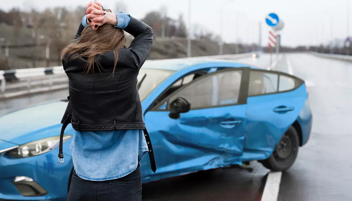 A woman holding her head next to a car accident.