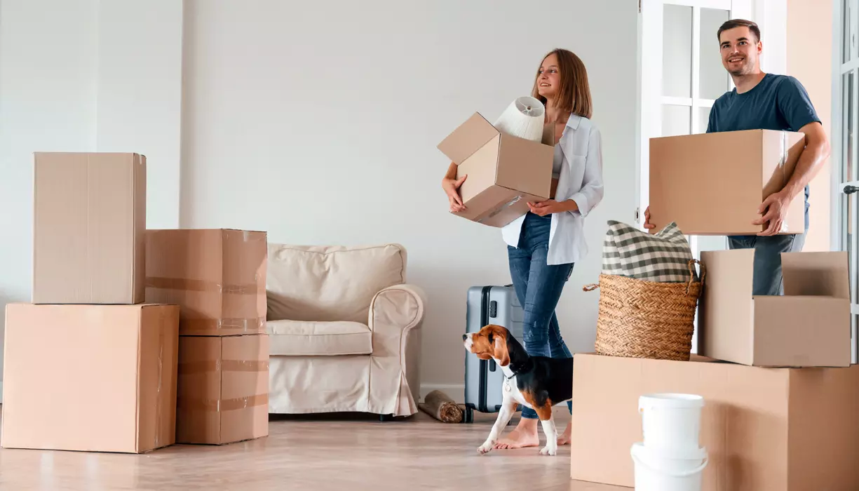 Two people and a dog walking into a room filled with moving boxes.