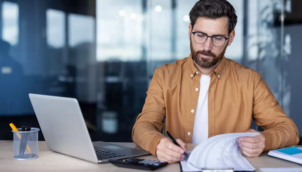 A man writing on a piece of paper next to a calculator.