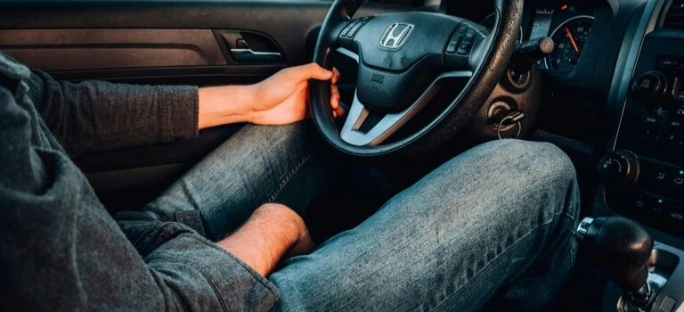 Driver sitting behind the wheel of a car, one hand resting casually on the steering wheel