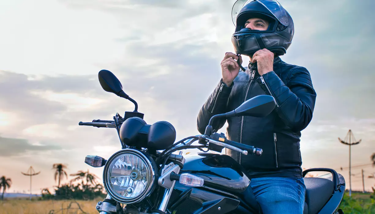 A man sitting on a motorcycle and putting his helmet on.